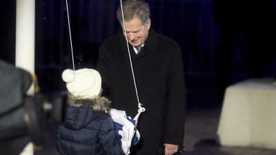 Sauli Niinistö med ett barn som ska dra upp Finlands flagga i flaggstången.