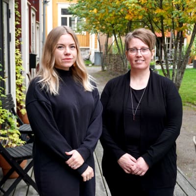 Två svartklädda kvinnor står på en veranda.