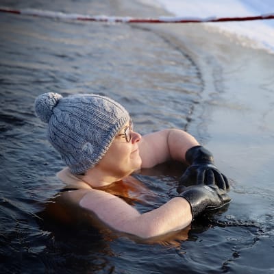 En kvinna med mössa och handskar stöder sig mot kanten av ett isvak.