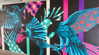 En väggmålning med stora fåglar i svart, blått och ljusrött.
