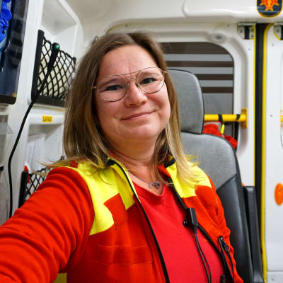 Kvinna i röda kläder sitter i en ambulans.