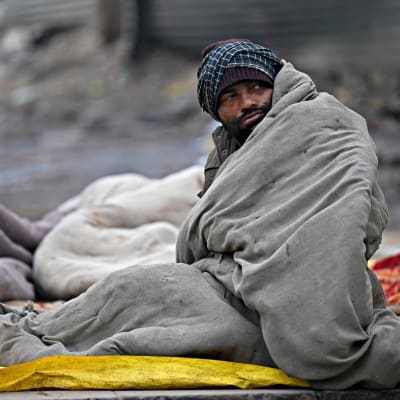 Peittoon kääriytynyt koditon mies istuu tien varrella kylmänä talviaamuna Delhissä 4. tammikuuta 2023.