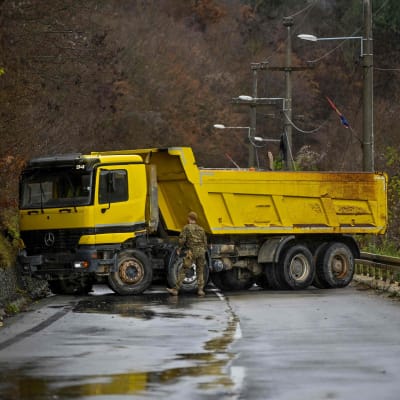 En soldat ur Natos KFOR-trupper inspekterar en gul lastbil som parkerats tvärs över en väg som vägspärr i Kosovo i mitten av december 2022.