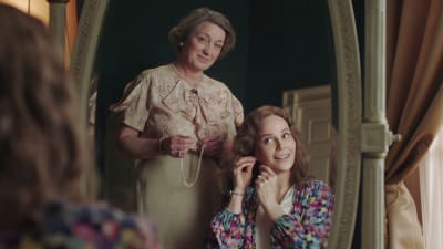 Spegelbild där kronprinsessan Märtha sitter vid ett sminkbord. Ragni står bakom med ett halsband i handen.