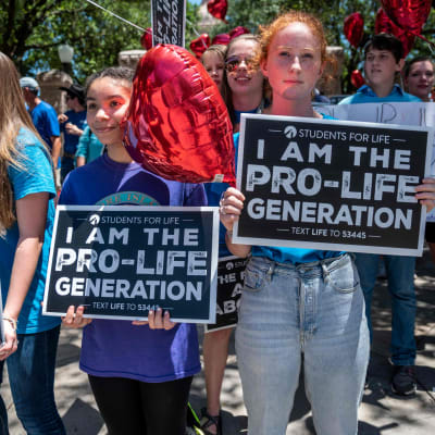 Tre flickor deltar i en demonstration mot abort, i bakgrunden fler deltagare.
