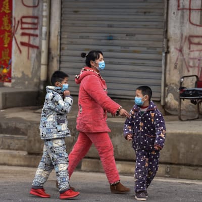 På bilden syns en mamma med sina två barn promenera i Wuhan iklädda ansiktsmasker.
