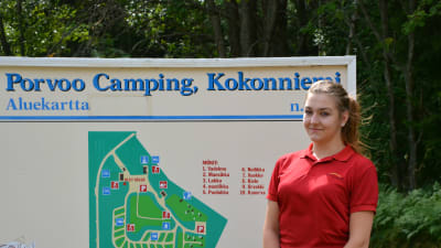 En kvinna i röd t-skjorta står framför skylt med karta över campingområdet.