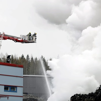 Vattenstråle riktas från en lyftkran ner mot ett moln av brandrök. Brandmän arbetar under en eldsvåda i Tammerfors den 11 maj 2020.