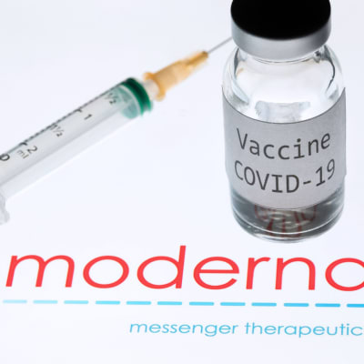 Flaska med vaccin samt en injektionsspruta på en vit yta med texten Moderna. 