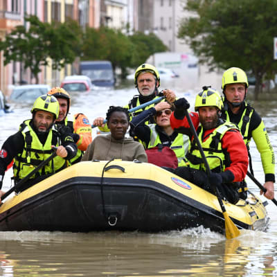 Räddningspersonal paddlar i en gummibåt på en översvämmad gata.