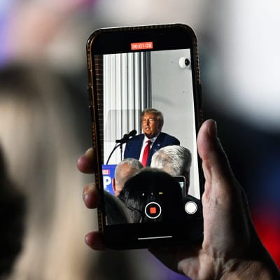 Yleisössä oleva henkilö kuvaa kännykällä videota Donald Trumpista hänen pitäessään puhetta Trump National Golf Club Bedminsterilla New Jerseyssä.