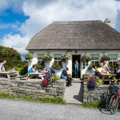 En pittoresk irländsk pub omgärdad av stenmur på landsbygden med folk på terrassen.