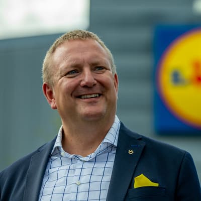 Lidls vd Lauri Sipponen i bildens vänstermiljö och i bakgrunden företagets logotyp. 