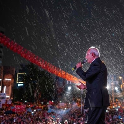 En man i kostym står på en scen i regn och för valkampanj.