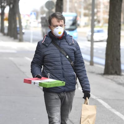 En man som har ett andningsskydd och håller i en pizzakartong ute på gatan.