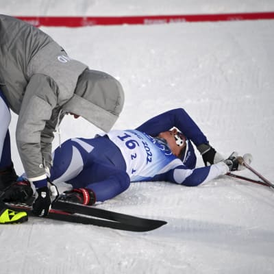 Kerttu Niskanen auttaa maassa makaavaa Krista Pärmäkoskea ottamaan sukset pois Pekingin olympialaisissa.
