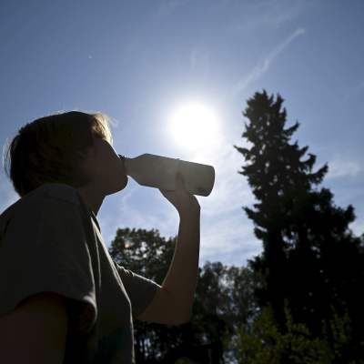 Ung människa dricker ur en flaska, i bakgrunden ljus blå himmel.