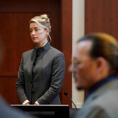 Amber Heard seisoo oikeudessa. Etualalla Johnny Depp epäterävänä.