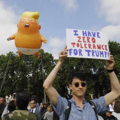 Trumpbaby ballong i luften med en demonstrant med en skylt.