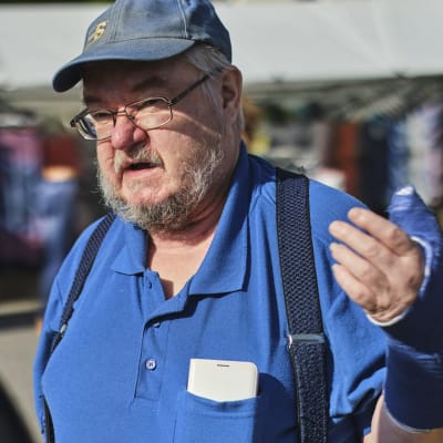 Sannfinländaren Pekka Kataja står på ett torg och pratar. Han håller ena armen uppe, den är täckt i gips. 