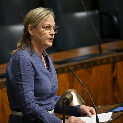 Riksdagsledamot Eva Biaudet står iklädd blått och talar i talarstolen i riksdagen.