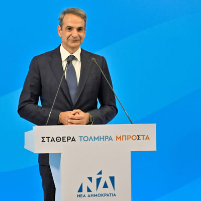 Kyriakos Mitsotakis står vid ett talarpodium och ser glad ut.