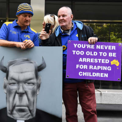 Demonstranter utanför domstolen i Melbourne med ett plakat där det står: "Du är aldrig för gammal för att gripas för våldtäkt av barn".