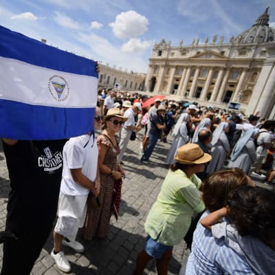 En man håller upp Nicaraguas flagga på Petersplatsen i Rom. Alla människor är vända mot Apostolska palatset, men påven syns inte på bilden.