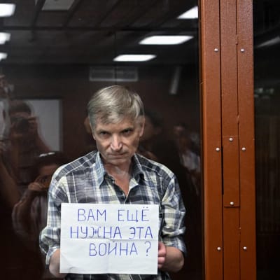 Alexei Gorinov näyttää oikeussalin istunnossa lasisellin takaa lappua, jossa lukee venäjäksi "Tarvitsetteko yhä tätä sotaa?".
