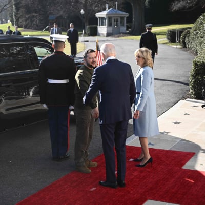 VOlodymyr Zelenskyj skakar hand med Joe Biden och hans fru på en röd matta framför en limousin.