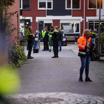 I förgrunden ser man en kvinna i reflexväst som kollar på någonting hon har i handen, i bakgrunden står poliser och väntar på någonting