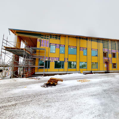 Värikäs koulurakennus, jonka päädyssä rakennustelineitä.