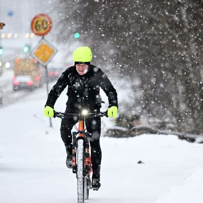 Henkilö pyöräilee lumisateessa.