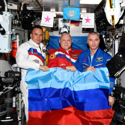 De ryska kosmonauterna Sergej Korsakov (till vänster), Oleg Artemijev och Denis Matvejev på Internationella rymdstationen ISS gratulerade de ryska styrkorna för att ha erövrat hela Luhansk-regionen.  På det här fotot som Roscosmos publicerade på måndagen, poserar de med flaggan för den självutropade Folkrepubliken Luhansk. 