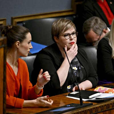 Sanna Marin, Annika Saarikko och Maria Ohisalo sitter vid ett bord i riksdagen.