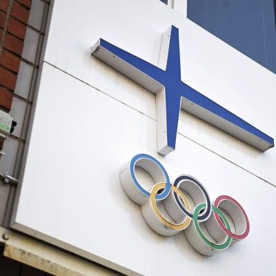 Olympiarenkaat ja Suomen lippua kuvastava sininen risti talon seinässä.