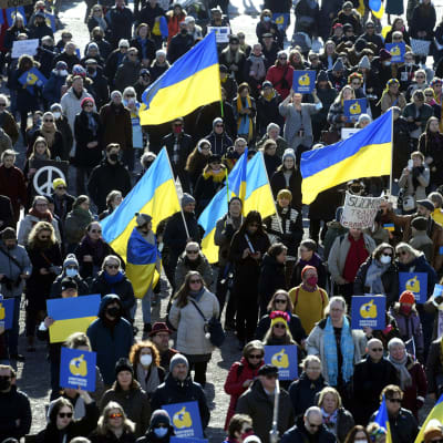 Mielenosoittajat pitelevät Ukrainan lippuja ja kylttejä Senaatintorilla.