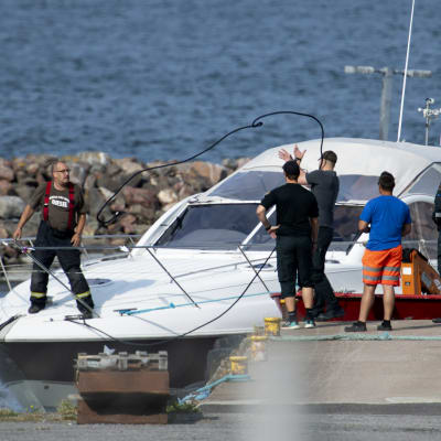 Större motorbåt vid brygga men människor kring och på båten. Olycksbåtarna på Erstan den 3 augusti 2019 transporterades till Pärnäs i Nagu.