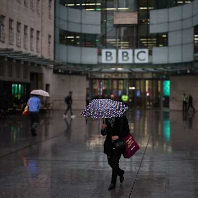  ihmiset kävelevät sateenvarjojen alla BBC:n rakennuksen edessä.