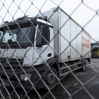 Lastbil med Postens logga står parkerad bakom ett stängsel.