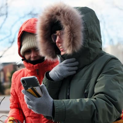 Två personer som har på sig tjocka vinterjackor med huvor neddragna över pannan. De har röda nästippar och det ser ut att vara kallt.
