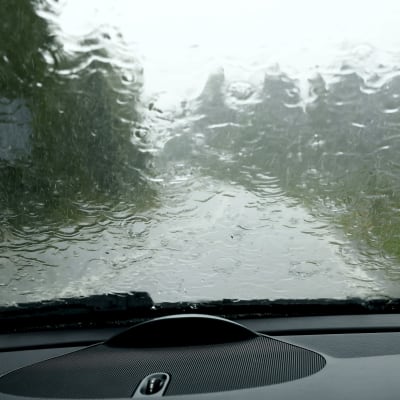 Kuva auton sisältä tuulilasista, johon sataa runsaasti vettä.