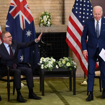 Anthony Albanese och Joe Biden träffas med amerikanska och australiska flaggor bakom sig. Albanese skrattar.