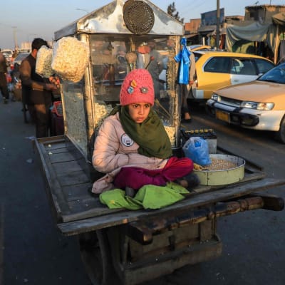 Nuori lapsi myymässä popcornia, odottamassa asiakkaita kadulla Kabulissa.
