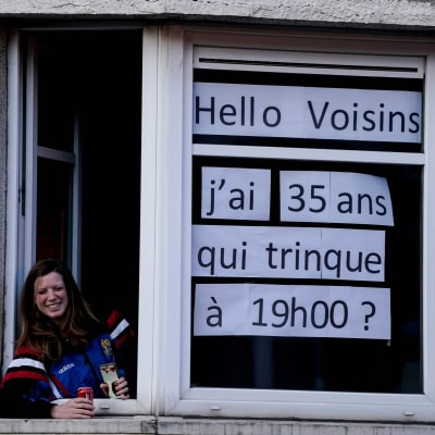 En kvinna med en skylt i fönstret där det står: Jag fyller 35 år i dag. Vem skålar med mig klockan 19. På grund av utegångsförbudet har belgier inte möjlighet att samlas i grupper. 