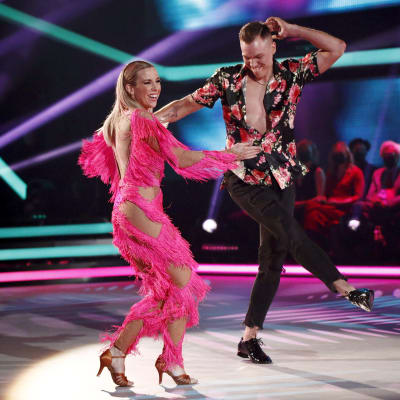 Kvinna i rosa dansdräkt ler och dansar på en scen med en man.