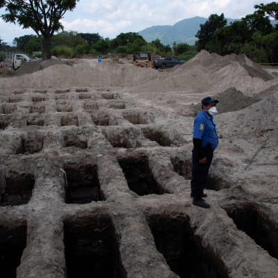 En polis i El Salvadors huvudstad San Salvador vid nygrävda gravar för pandemioffer. Bilden är tagen den 27 juli. 