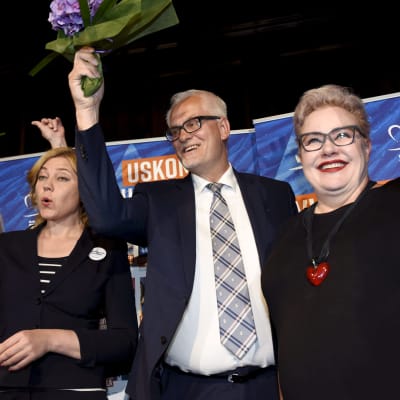 Henna Virkkunen, Petri Sarvamaa och Sirpa Pietikäinen jublar med blommor i händerna.