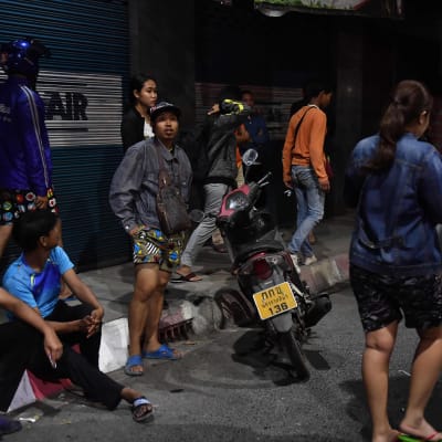 Personer sitter på trottoarkanten i Korat i Thailand. 