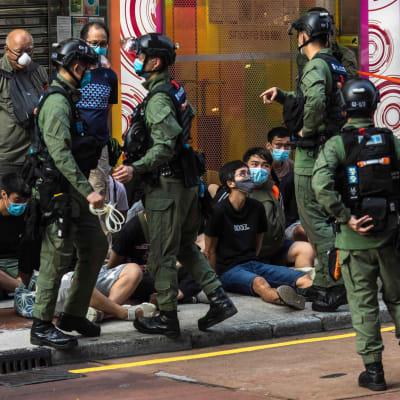 Poliser på gata i Hongkong, på marken sitter unga personer.